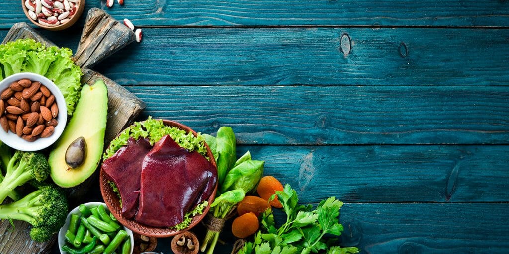 Food containing natural iron. Fe: Liver, avocado, broccoli, spinach, parsley, beans, nuts, on a blue background. Top view.